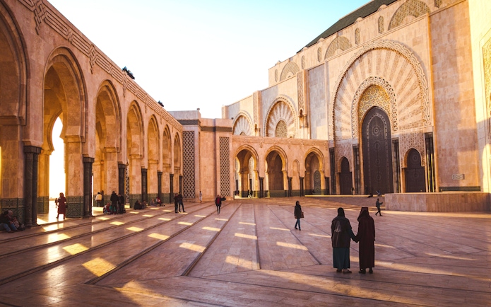 Ornate brass door and arches of Hassan II Mosque, Casablanca, Morocco, with people in courtyard.