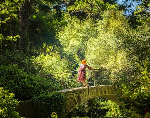 Girl walking along lush green garden pathway at Quinta Da Regaleira, Lisbon.
