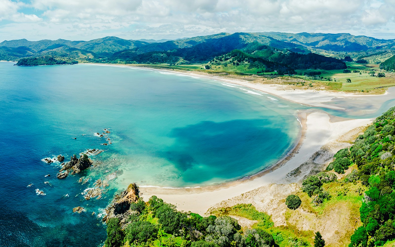 Aerial view of Waikawau Beach with lush greenery and clear blue waters, Waitomo, New Zealand.