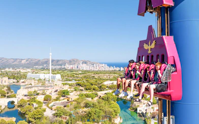Visitors on a drop tower ride at Terra Mitica Benidorm with cityscape in the background.