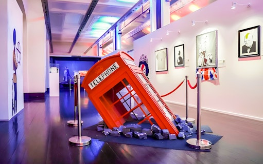 Banksy exhibit with a tilted red telephone booth installation and framed artworks.