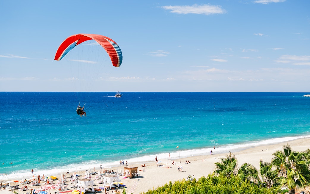 Paragliders soaring over Alanya beach with turquoise sea in the background.