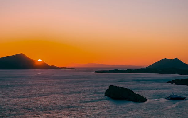 Sunset over Cape Sounion with a yacht on the Aegean Sea.