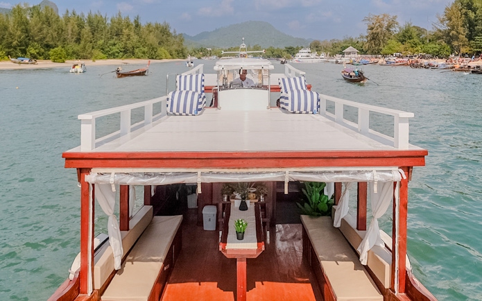 Upper deck of a long tail boat in Krabi with striped cushions and scenic view.