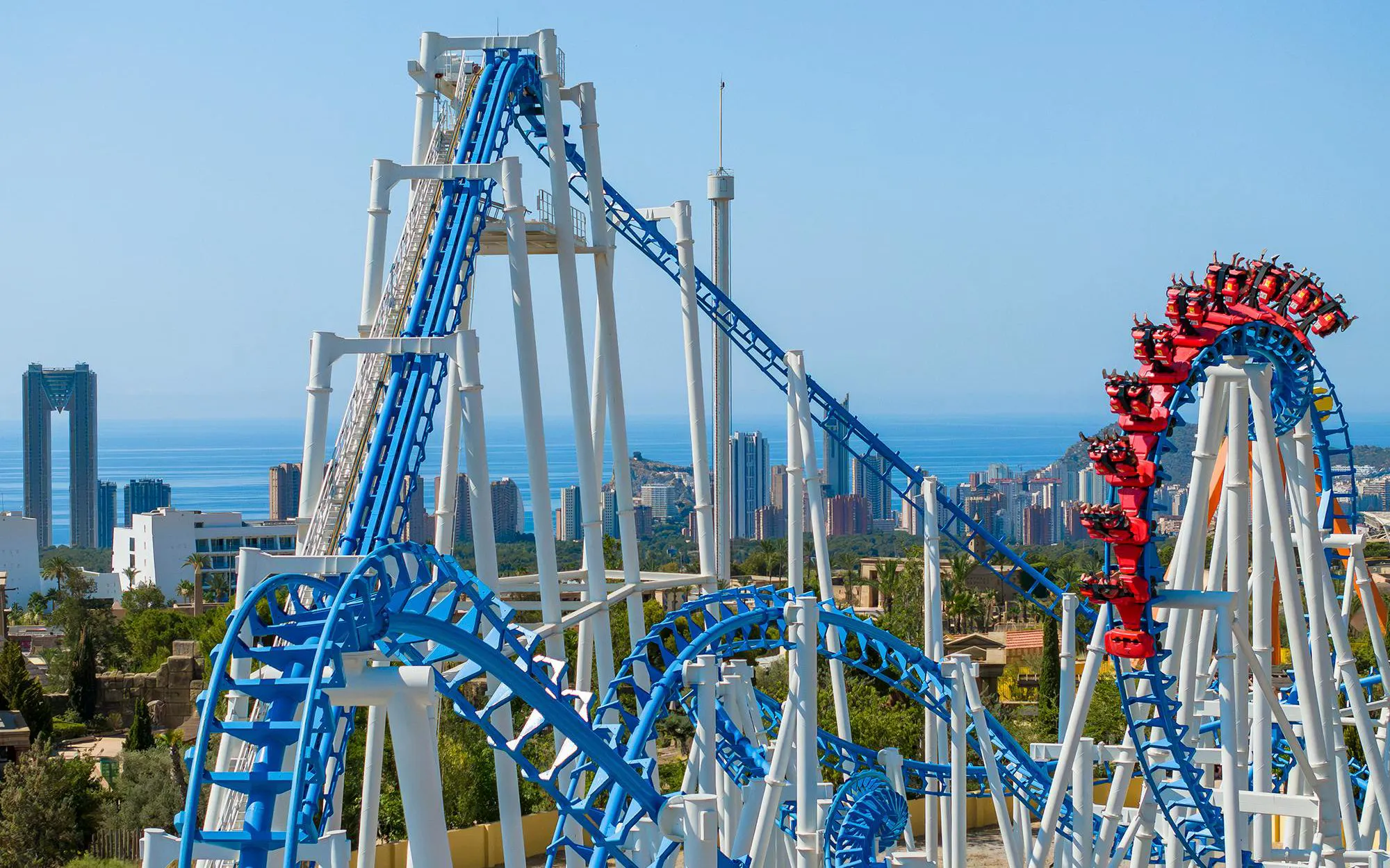 Roller coaster at Terra Mitica theme park in Spain with city skyline in background.