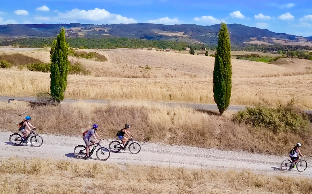 Cyclists on e-bikes ride through Chianti countryside near Florence, flanked by cypress trees.