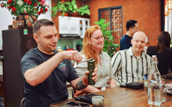 Participants at Hanoi coffee workshop preparing brew with manual grinder.