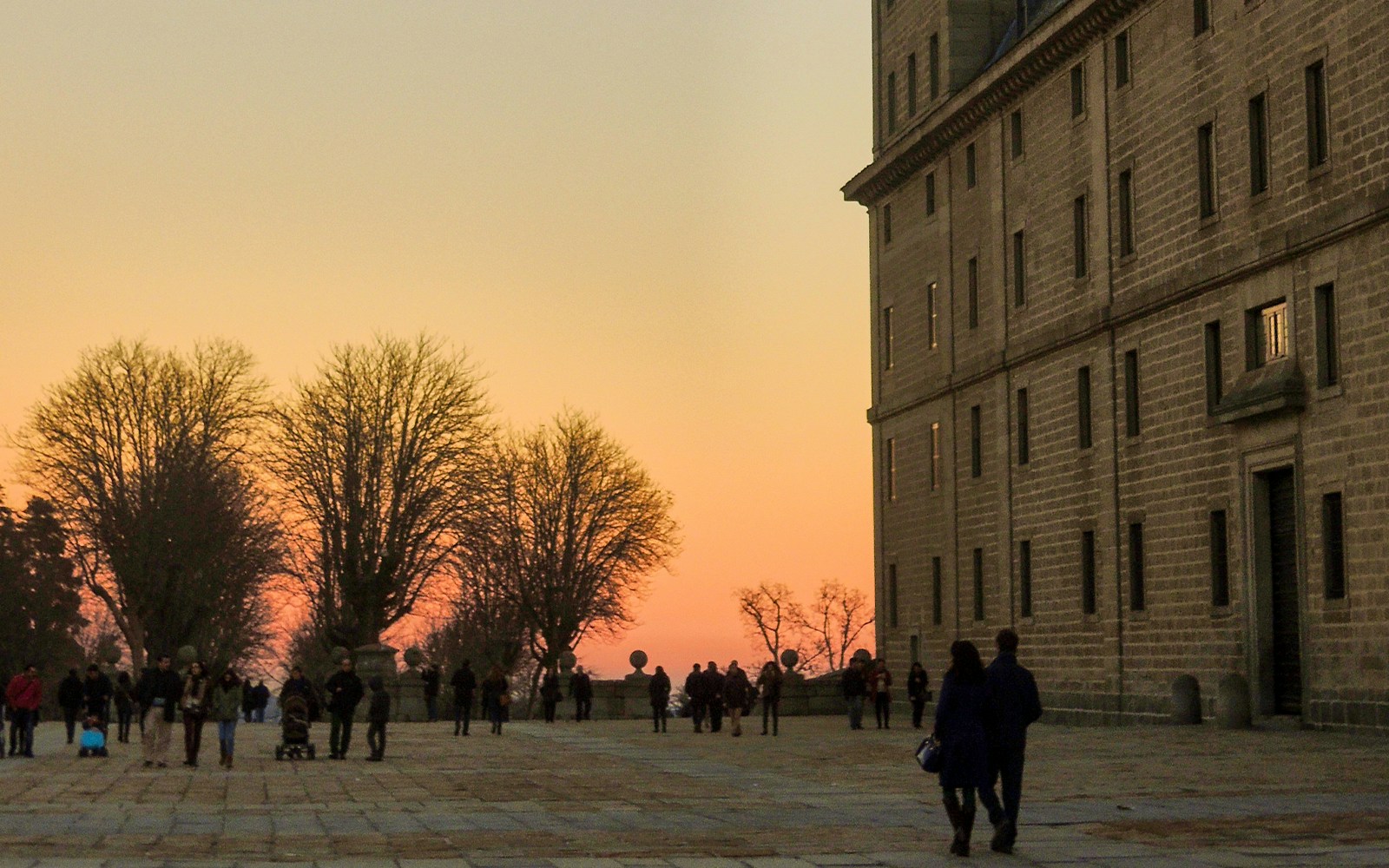 El Escorial at sunset with people walking along the courtyard.