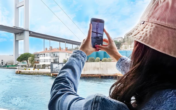 Person photographing Bosphorus Bridge from a boat during a cruise in Istanbul.