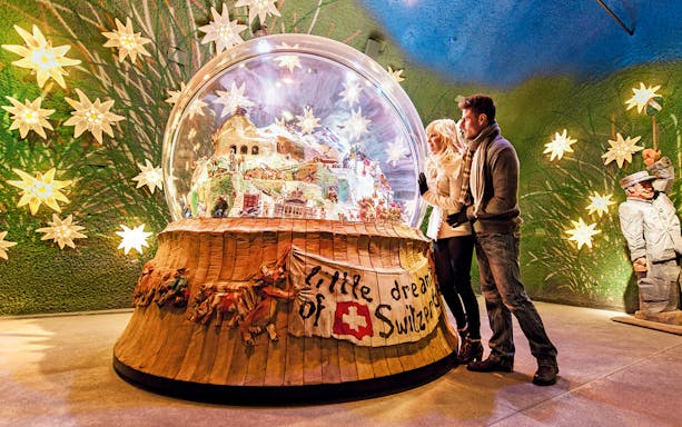 Couple admiring a large snow globe display at a museum in Jungfraujoch, Switzerland.