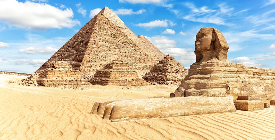 The Great Sphinx and Pyramids of Giza under a blue sky in Egypt.
