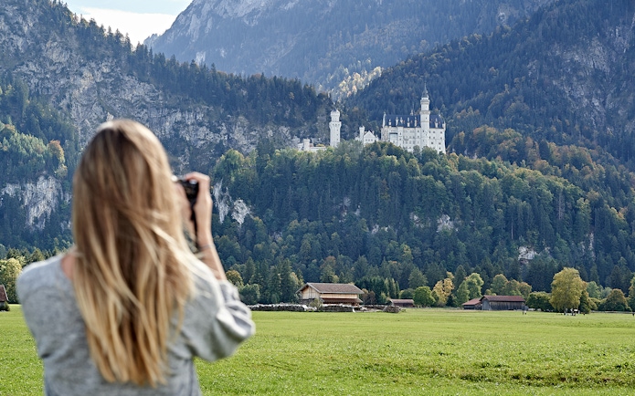 Person photographing Neuschwanstein Castle from a field, Bavaria, Germany.