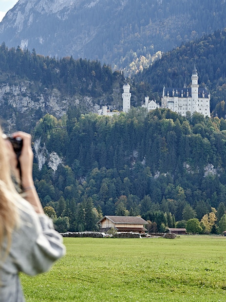 Person photographing Neuschwanstein Castle from a field, Bavaria, Germany.