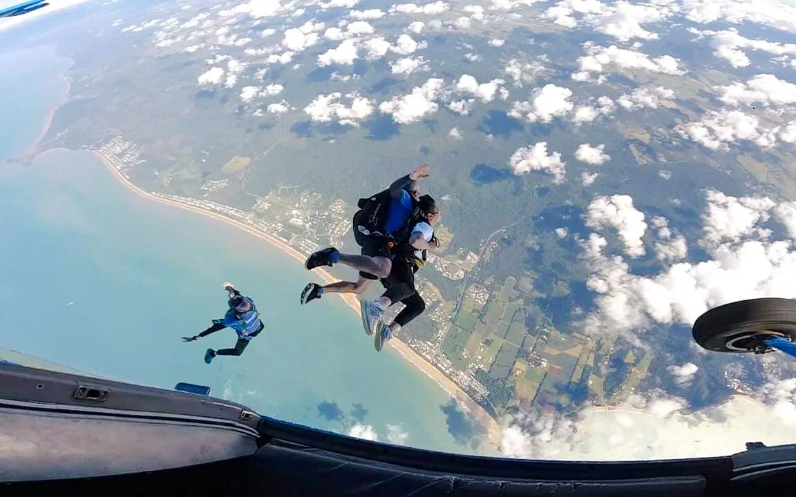 Skydivers tandem jumping over Mission Beach coastline.