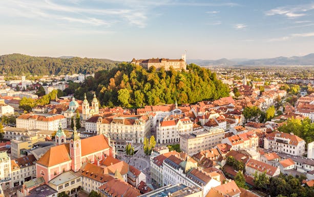 Panoramic view of Ljubljana with Ljubljana Castle on a hill surrounded by historic buildings.