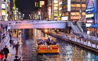 Tombori River Cruise boat passing under a bridge in Dotonbori, Osaka at night.