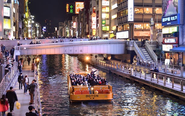 Tombori River Cruise boat passing under a bridge in Dotonbori, Osaka at night.