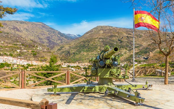 Cannon and Spanish flag at Visillo viewpoint, Lanjaron, Granada, with mountain backdrop.