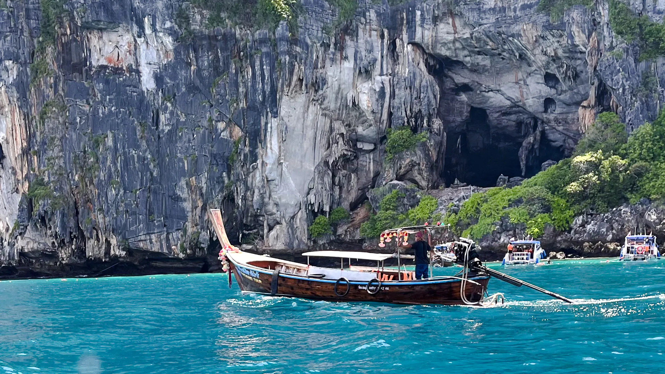 Private long-tail boat on turquoise waters near limestone cliffs, Koh Phi Phi, Krabi.