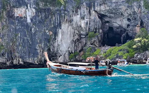 Private long-tail boat on turquoise waters near limestone cliffs, Koh Phi Phi, Krabi.