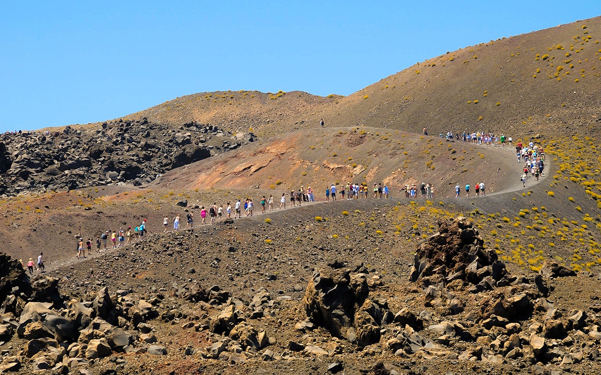 Tourists hiking on Nea Kameni volcano trail in Santorini, Greece.