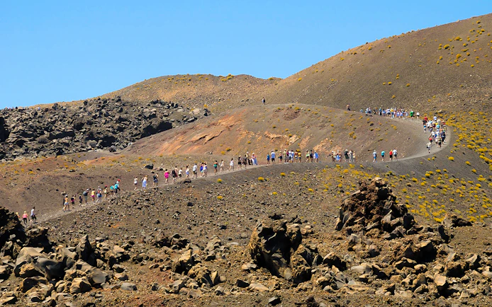 Tourists hiking on Nea Kameni volcano trail in Santorini, Greece.
