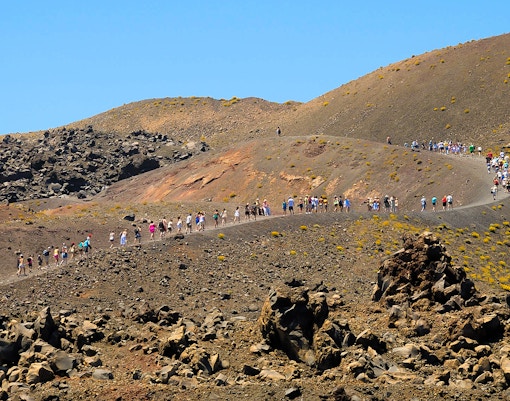 Tourists hiking on Nea Kameni volcano trail in Santorini, Greece.