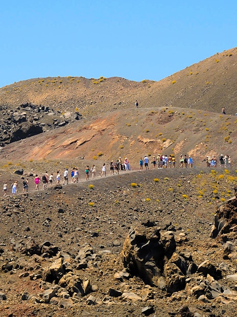 Tourists hiking on Nea Kameni volcano trail in Santorini, Greece.
