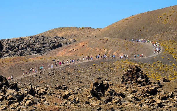Tourists hiking on Nea Kameni volcano trail in Santorini, Greece.