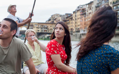 Guided boat tour on a Florentine gondola with tourists on the Arno River.