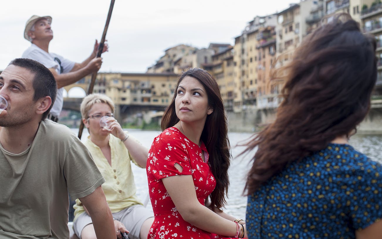 Guided boat tour on a Florentine gondola with tourists on the Arno River.