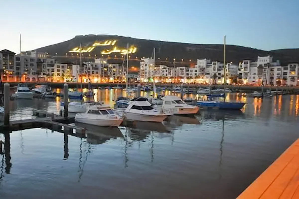 Boats docked at Agadir marina with illuminated hillside in the background.