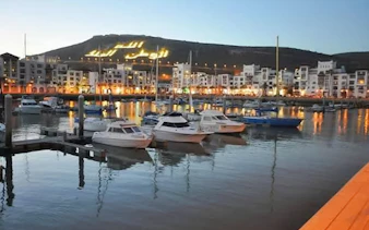 Boats docked at Agadir marina with illuminated hillside in the background.