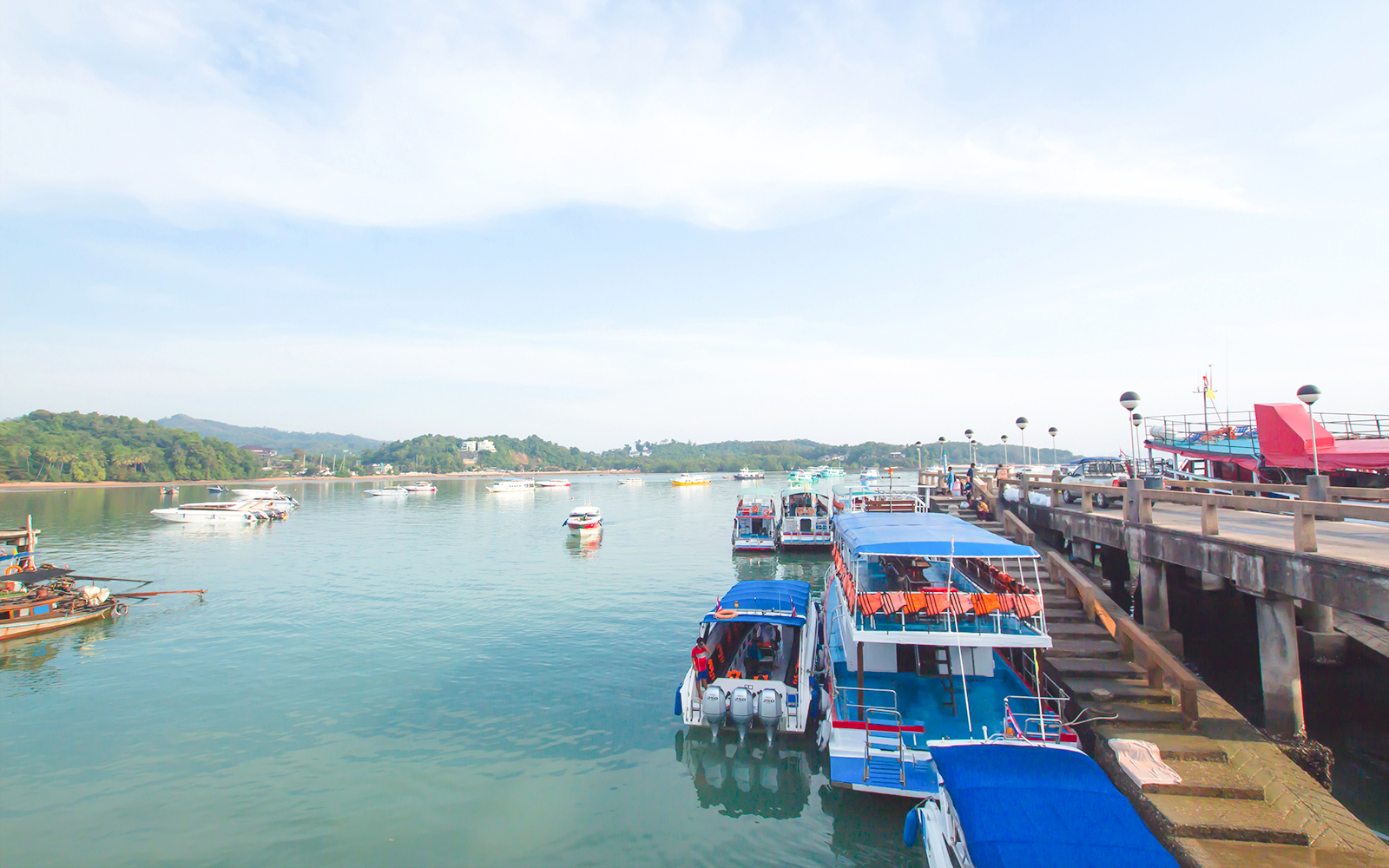 Boats docked at Koh Naka Noi Beach pier, Phuket, Thailand, with Naka Island in the background.