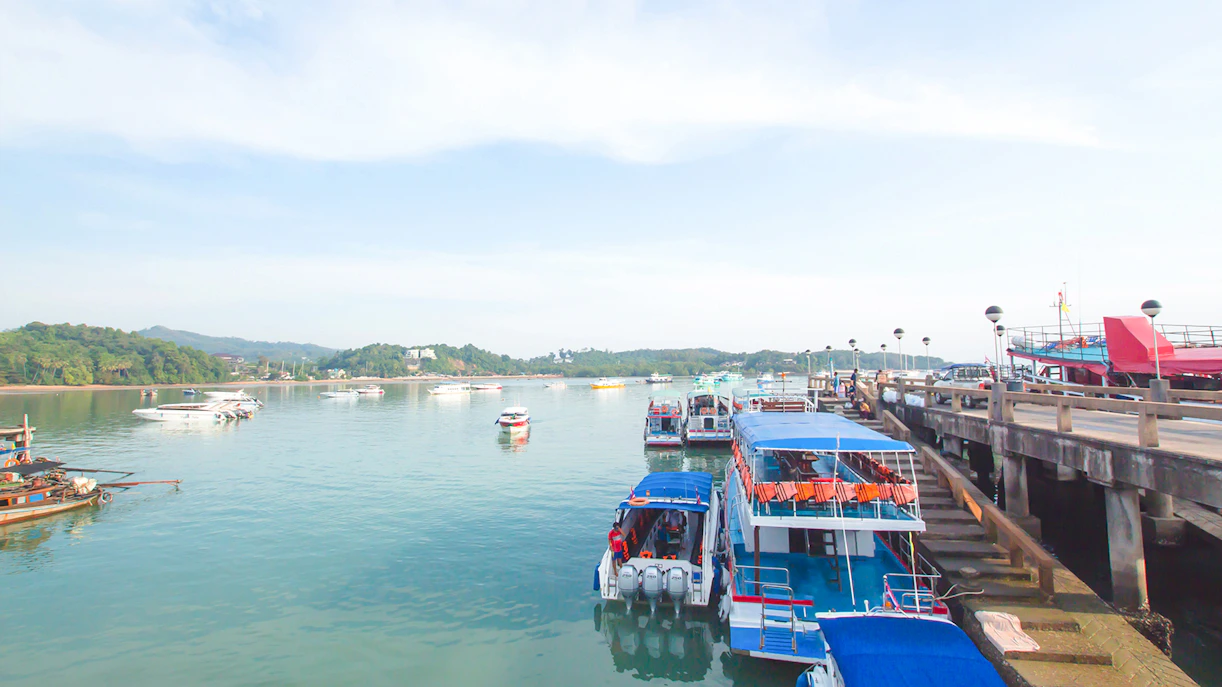 Boats docked at Koh Naka Noi Beach pier, Phuket, Thailand, with Naka Island in the background.