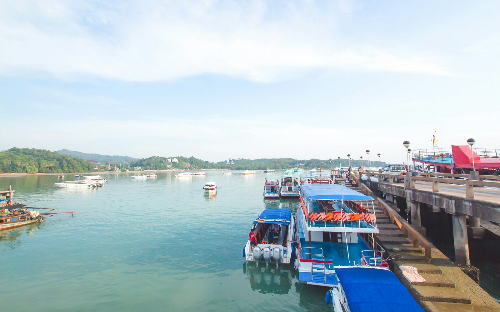 Boats docked at Koh Naka Noi Beach pier, Phuket, Thailand, with Naka Island in the background.