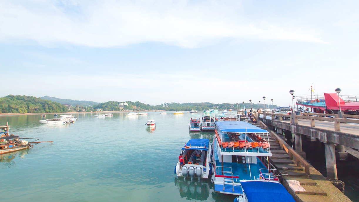 Boats docked at Koh Naka Noi Beach pier, Phuket, Thailand, with Naka Island in the background.