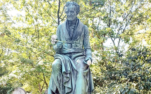 Père Lachaise Cemetery statue in Paris, France, surrounded by trees and gravestones.