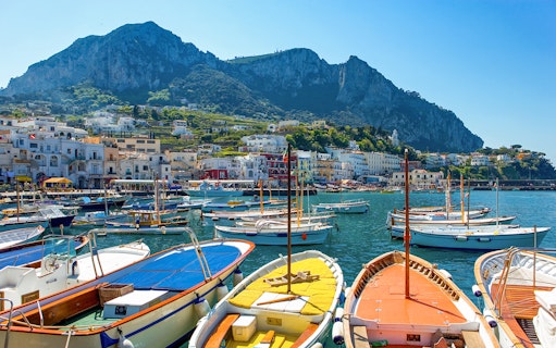 Boats moored at Capri dock with town and cliffs in the background, Italy.