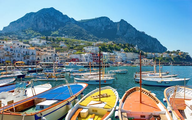 Boats moored at Capri dock with town and cliffs in the background, Italy.