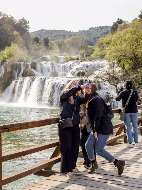 Tour group taking photos at Krka river waterfall, Krka National Park.