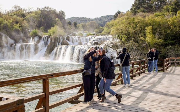 Tour group taking photos at Krka river waterfall, Krka National Park.