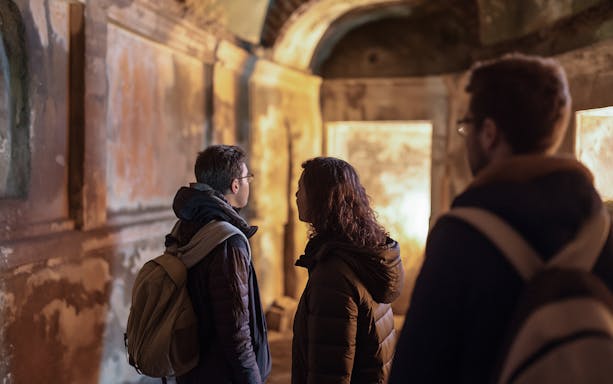 Visitors exploring underground Roman catacombs on a guided tour.