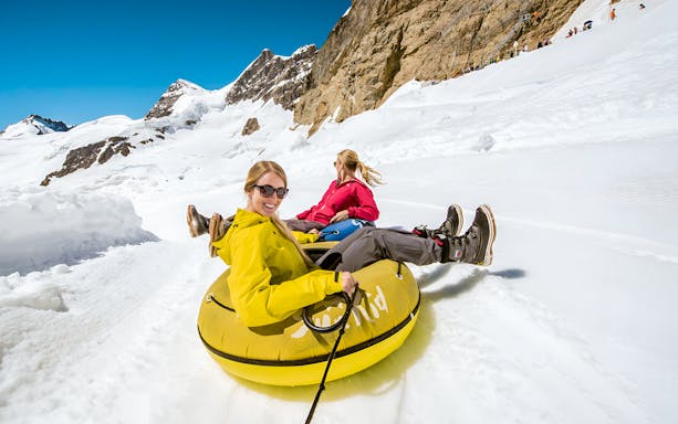 People snow tubing on a snowy slope in Interlaken with mountain views.