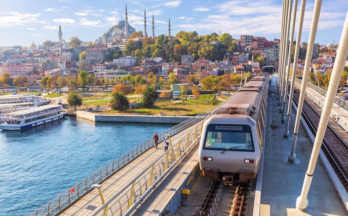 Istanbul metro train crossing bridge with cityscape and mosque in the background.