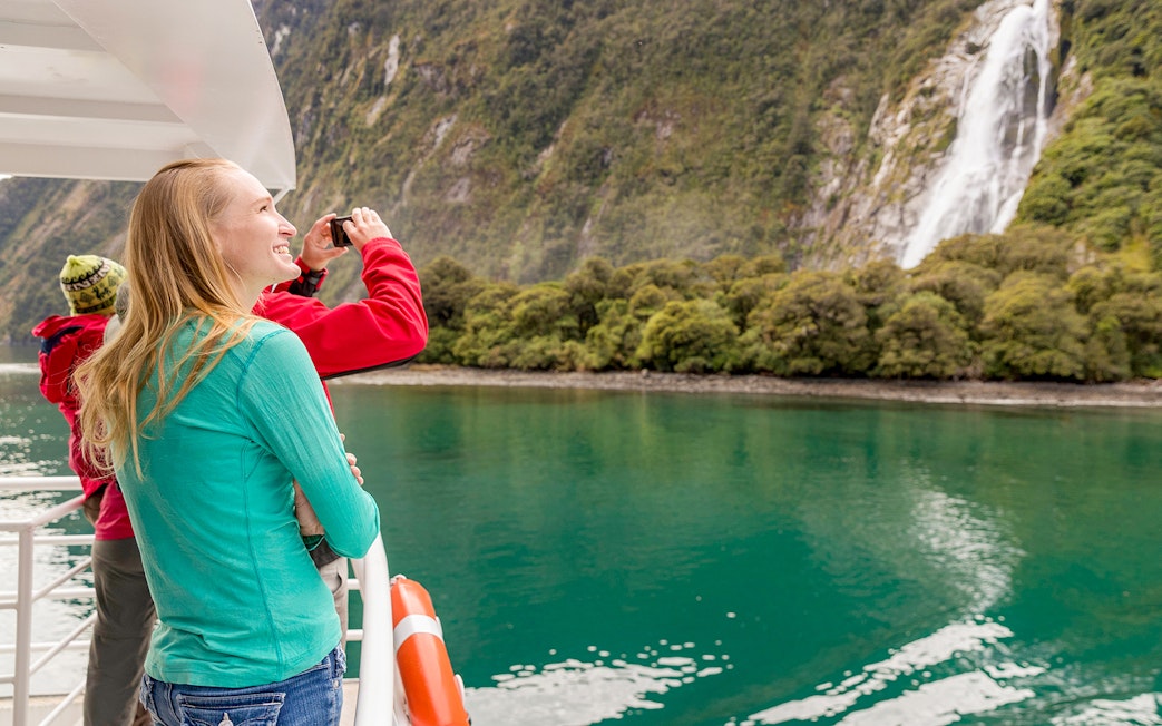 People enjoying Milford Sound cruise with waterfall view in New Zealand.
