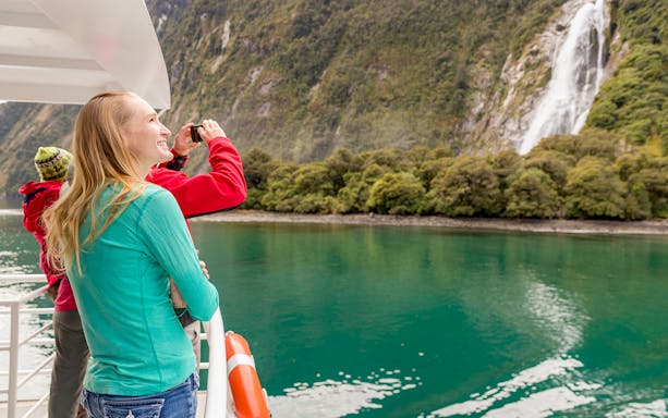 Milford Sound cruise passengers viewing fjords and waterfalls, New Zealand.