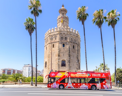 Turistas desfrutando de uma oferta combinada de passeio de ônibus Hop on hop off Sevilha e ingressos para o parque temático Isla Mágica, mostrando a bela paisagem urbana de Sevilha e atrações divertidas