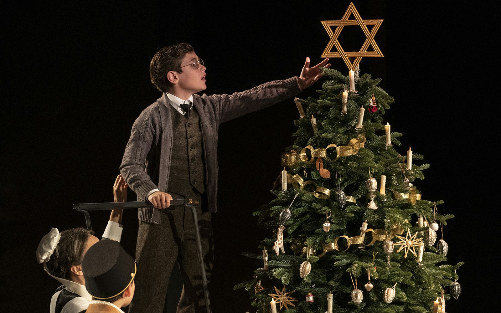 Child reaching to place a Star of David on a decorated Christmas tree in Leopoldstadt.