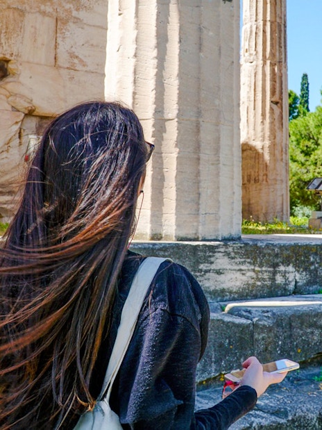 Woman using audio guide at Ancient Agora ruins in Athens.